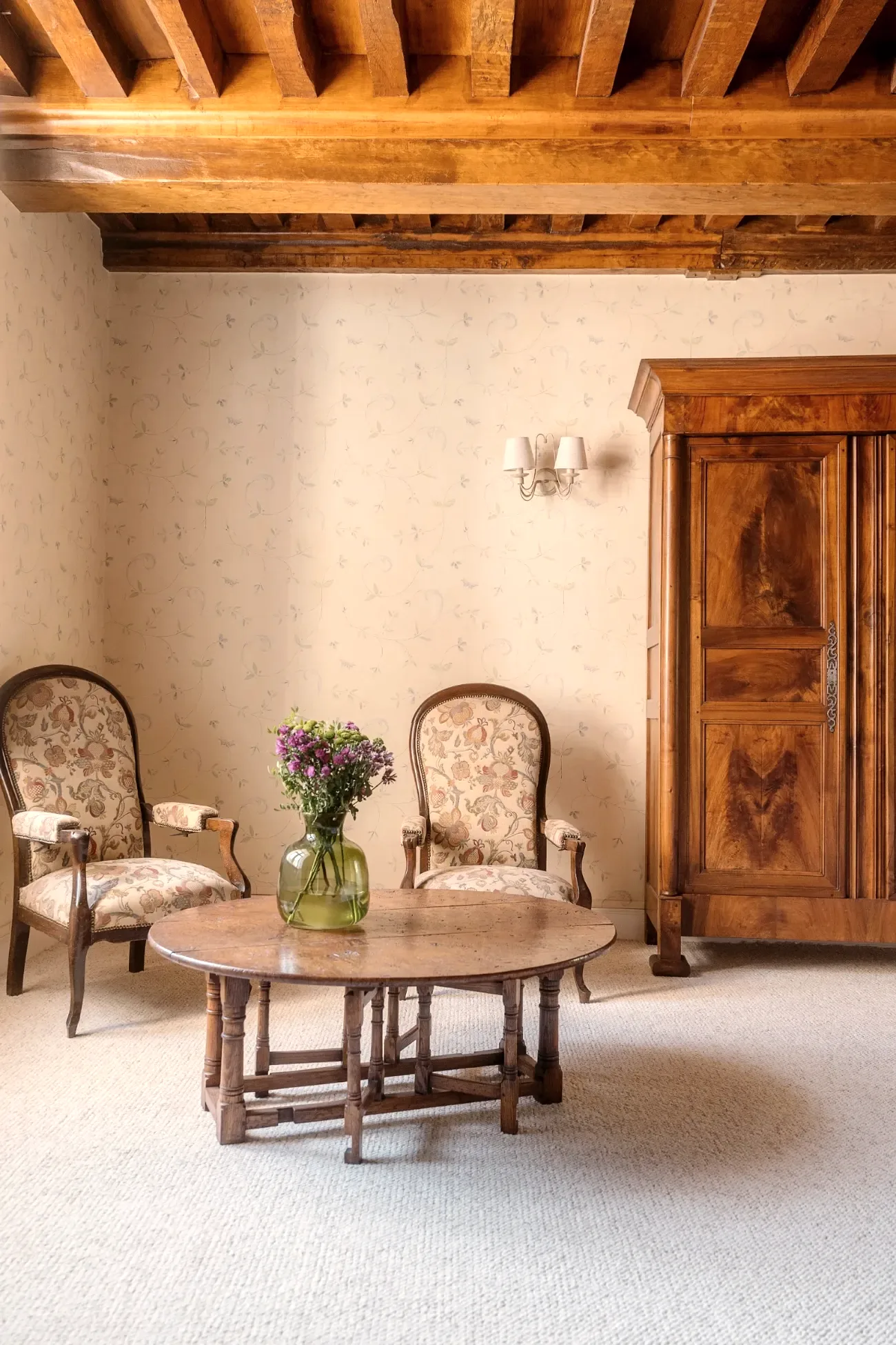 Coin salon d'une chambre, fauteuils fleuris et poutres apparentes